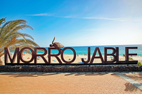 Blick auf den Schriftzug Morro Jable mit Strand und Meer im Hintergrund